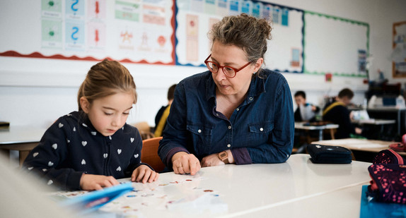 Eine Schülerin und eine Lehrerin an einem Tisch in einem Schulraum