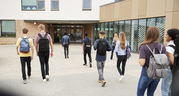 Erwachsene und jugendliche Schülerinnen und Schüler gehen in ein Schulgebäude