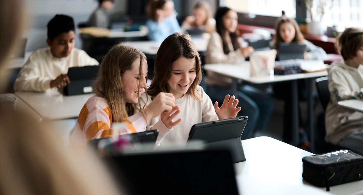 Zwei Schülerinnen sitzen im Unterricht. Sie arbeiten gemeinsam an einem Tablet.
